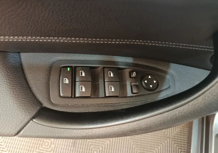 Gros plan sur les commandes de lève-vitres et rétroviseurs côté gauche d'une BMW X1 2019 finition M Sport.