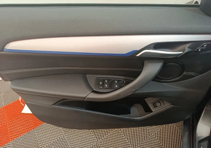 Vue intérieure côté gauche de la porte BMW X1 sDrive18i M Sport avec garniture noire et insert clair, commandes fenêtres visibles.