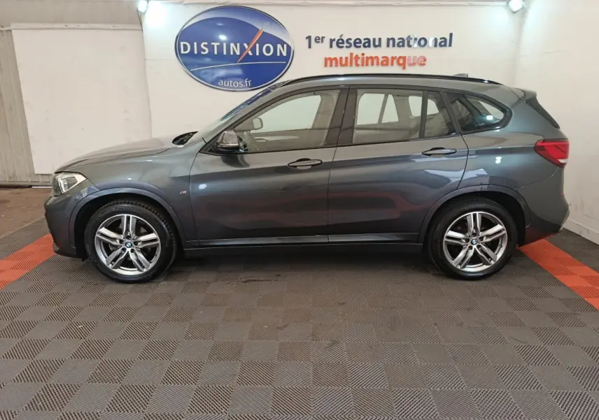 BMW X1 sDrive18i M Sport gris, vue profil côté gauche, avec jantes alliage et toit noir en intérieur showroom.