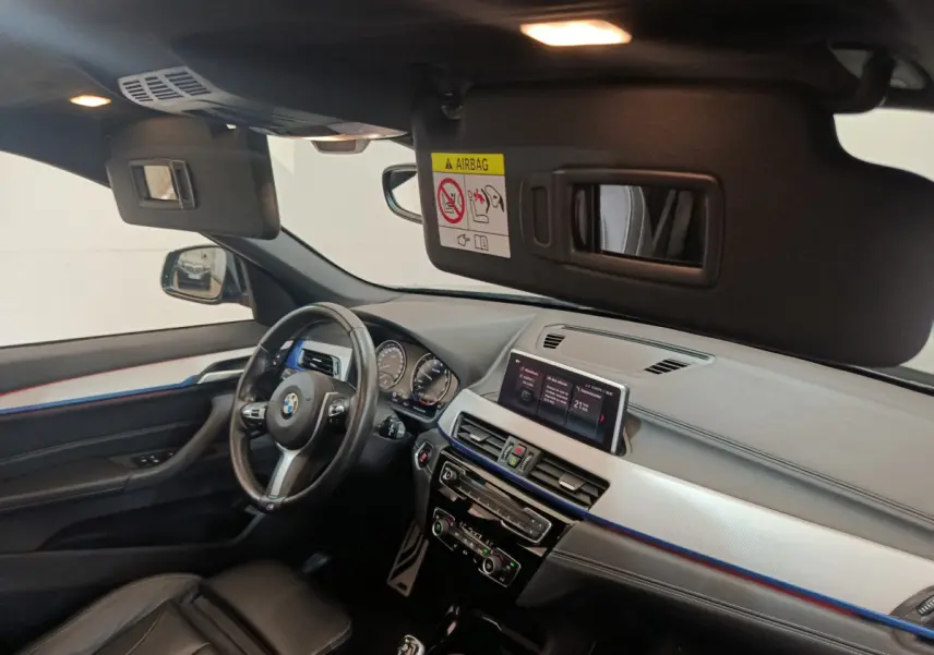 Intérieur BMW X1 sDrive18i 2019 vu côté conducteur, tableau de bord noir avec écran tactile et volant cuir.