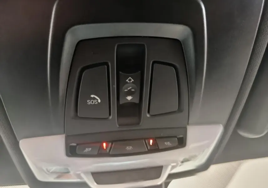 Vue en gros plan du panneau de commandes au plafond intérieur du BMW X1 sDrive18i M Sport 2019, avec bouton SOS et éclairage activé.