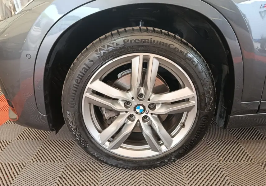 Gros plan sur la roue avant gauche grise d’un BMW X1 sDrive18i M Sport avec jante alliage et logo BMW visible au centre.