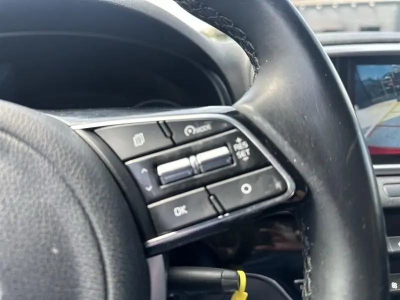 Gros plan sur les commandes au volant côté gauche du Kia Sportage 2021, avec écran de caméra de recul en arrière-plan.