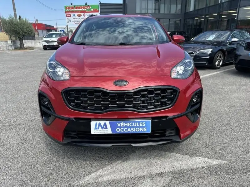 Vue de face d'un KIA SPORTAGE rouge métal 2021 avec calandre noire et plaque "Véhicules Occasions" visible.