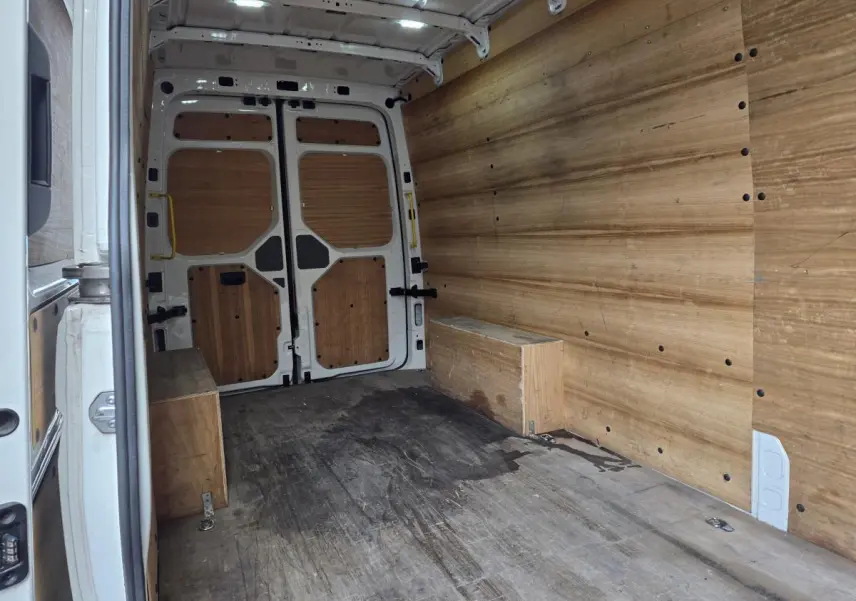 Intérieur du fourgon Volkswagen Crafter blanc vu de l'arrière, avec plancher et parois en bois clair.