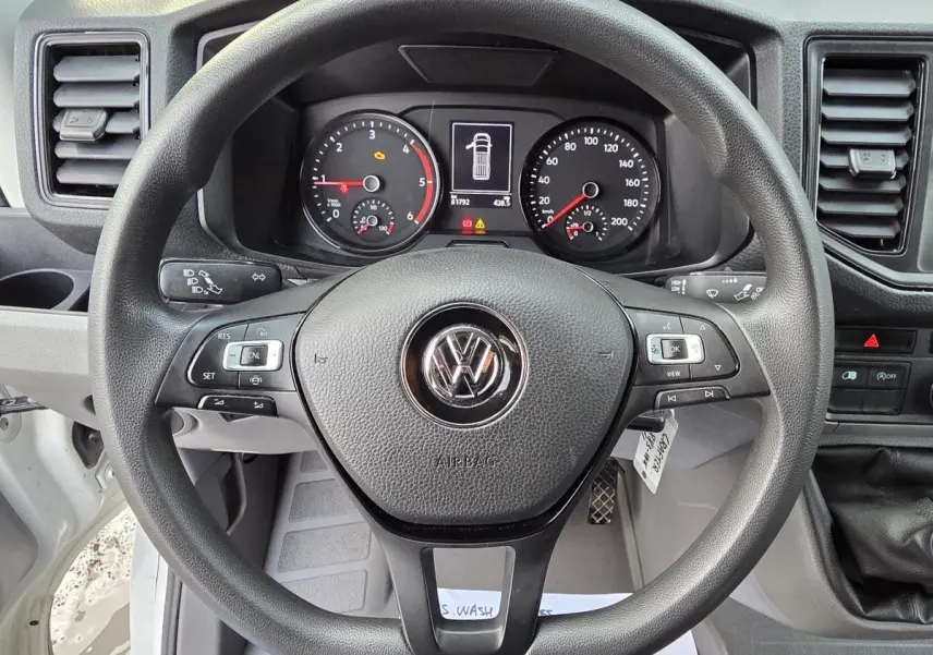 Vue rapprochée du volant multifonctions noir et du tableau de bord du Volkswagen Crafter Fourgon blanc 2023.