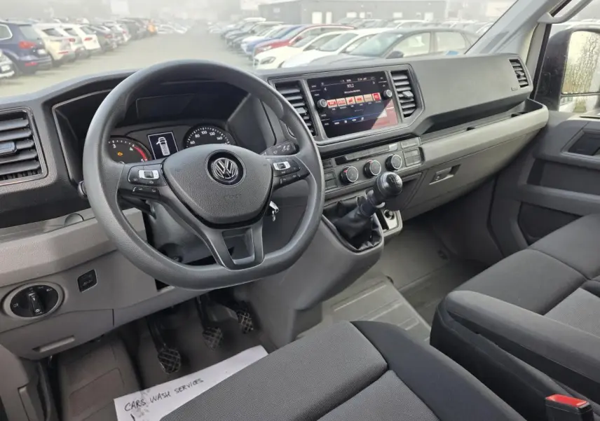 Intérieur avant du Volkswagen Crafter blanc 2023, tableau de bord noir avec volant multifonctions et boîte manuelle.
