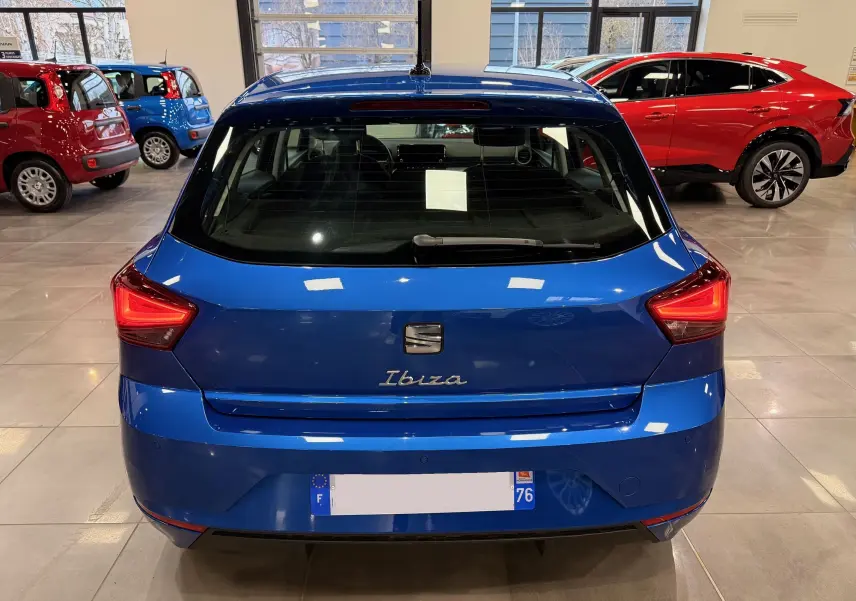 Vue arrière d'une SEAT Ibiza 2025 bleu vif, avec feux arrière allumés en forme triangulaire, dans un showroom lumineux.