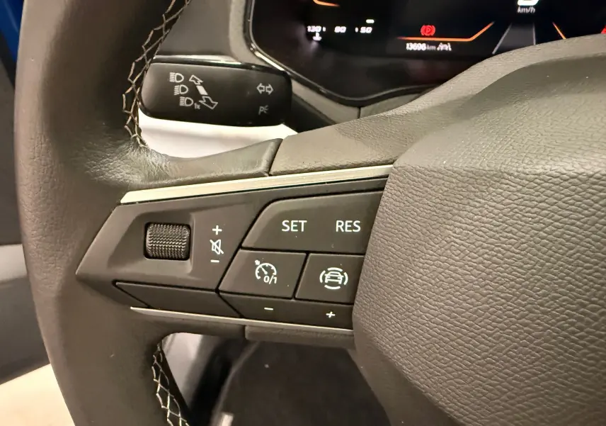 Gros plan sur les commandes au volant du SEAT Ibiza 2025, version 1.0 TSI Copa, avec tableau de bord numérique en arrière-plan.