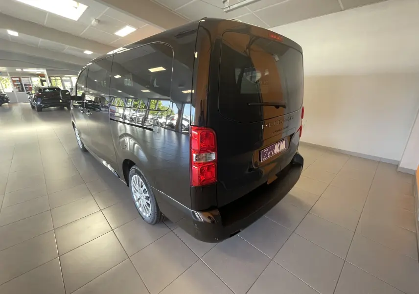 Vue 3/4 arrière droite du Peugeot Traveller noir 2026 en showroom, avec vitres teintées et feux arrière rouges.