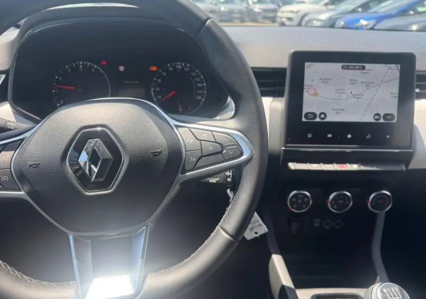 Intérieur Renault Clio 2023 vu du poste de conduite, volant multifonction et écran tactile avec navigation visible.