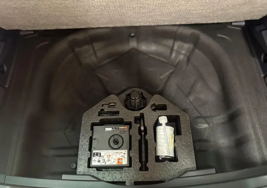 Coffre ouvert d'un SEAT Ateca 2.0 TDI 150 DSG7 Copa 2025 gris graphite, montrant le kit de réparation pneus rangé.