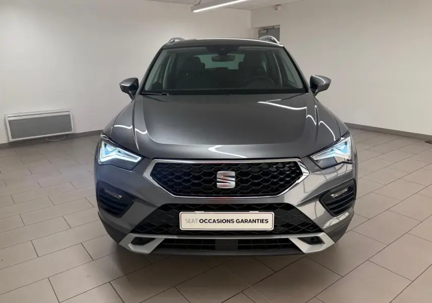 Vue frontale d'un SEAT Ateca gris graphite 2025 avec calandre hexagonale et phares LED allumés dans un showroom.