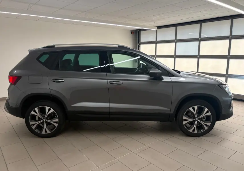 Vue de profil droit du SEAT Ateca 2025 gris graphite avec jantes alliage 18 pouces et toit noir en intérieur showroom.