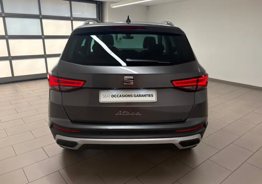 Vue arrière d'un SEAT Ateca 2.0 TDI gris graphite avec feux allumés et hayon électrique en intérieur showroom.