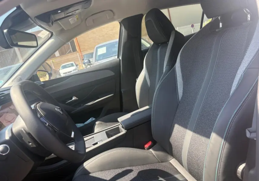 Vue intérieure côté conducteur du Peugeot 308 PHEV 180 e-EAT8 Allure 2024, sièges tissu et cuir gris, volant multifonction.
