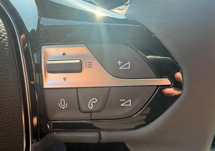 Gros plan sur les commandes multifonctions du volant de la Peugeot 308 PHEV 180 e-EAT8 Allure 2024 gris clair.