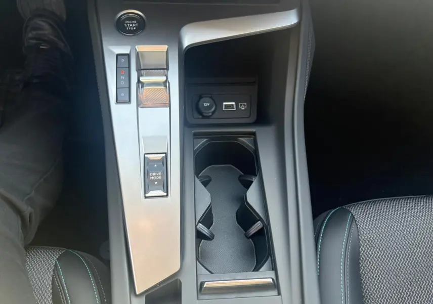 Vue plongeante sur la console centrale de la Peugeot 308 PHEV 180 e-EAT8 Allure 2024, avec levier de vitesses et porte-gobelets.