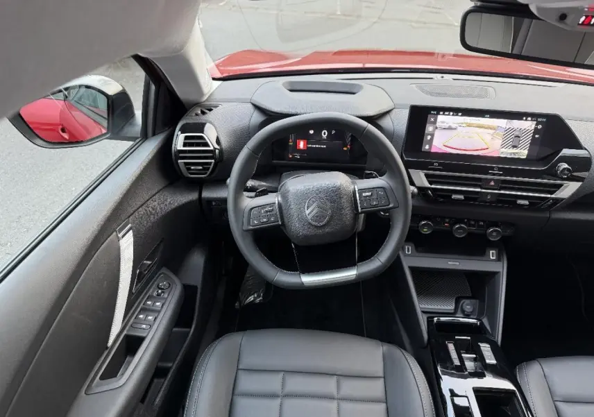 Intérieur de la Citroën C4 2025 rouge elexir, vue du poste de conduite avec volant multifonction et écran tactile central.