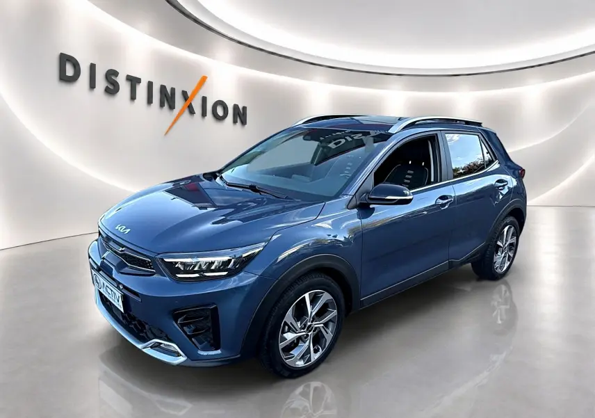 KIA Stonic gris en vue 3/4 avant droit, avec jantes alu et barres de toit visibles en showroom lumineux.