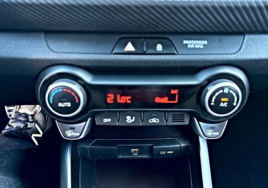 Vue rapprochée de la console centrale noire du Kia Stonic 2025, avec commandes de climatisation et ports USB/12V visibles.