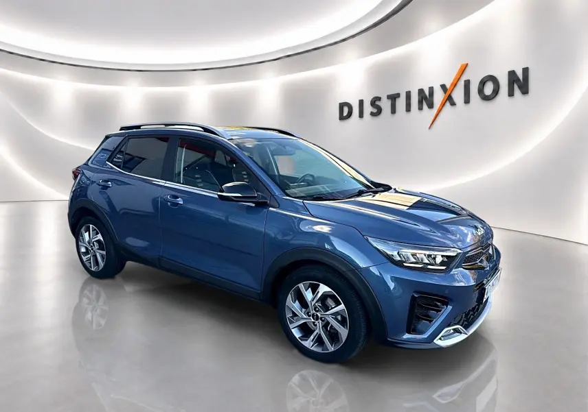 KIA Stonic gris en vue 3/4 avant droit, avec jantes alliage et barres de toit visibles dans un showroom lumineux.