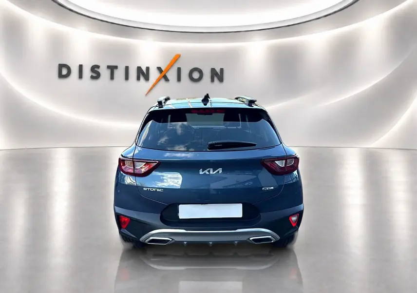 Vue arrière d'un KIA Stonic gris avec double sortie d'échappement et barres de toit dans un showroom lumineux.