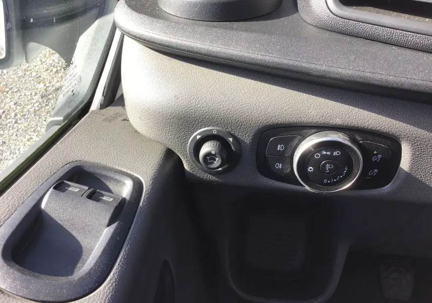 Détail intérieur côté gauche du tableau de bord du Ford Transit blanc, avec commandes d'éclairage et boutons de vitres électriques.