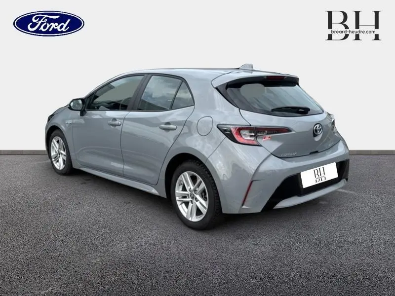 Toyota Corolla 122h Dynamic Business gris Manhattan métallisé vue 3/4 arrière droit avec feux LED et jantes alu.
