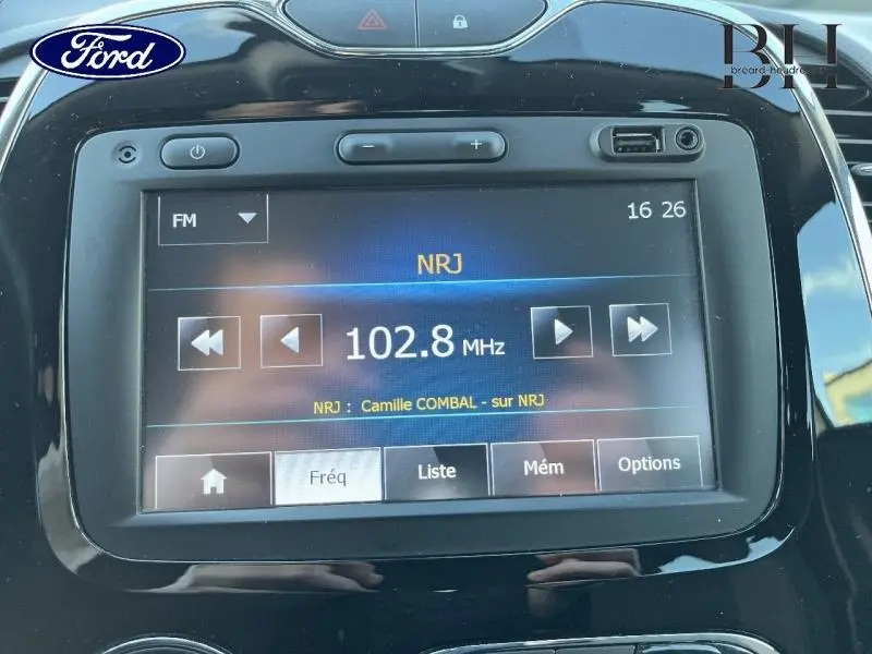 Écran tactile multimédia du tableau de bord d'une Renault Captur beige avec toit noir, affichant la radio NRJ 102.8 MHz.
