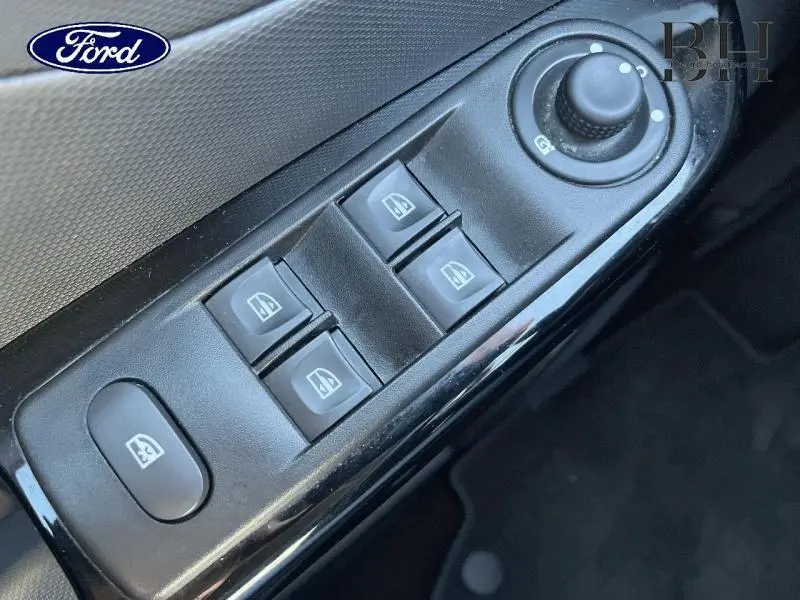 Gros plan sur les commandes de lève-vitres et rétroviseurs électriques côté conducteur, finition noire brillante.