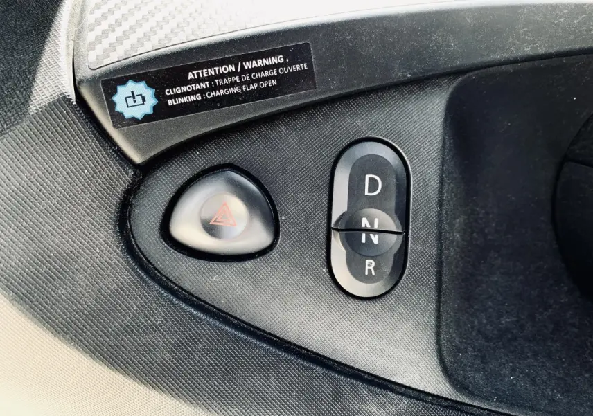 Gros plan sur la commande de boîte automatique et le bouton de warning dans l'habitacle noir d'une Renault Twizy blanche.