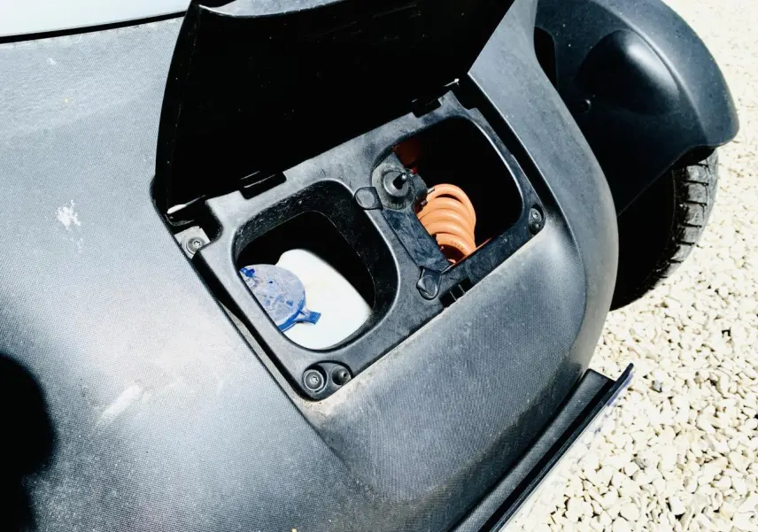 Gros plan sur la trappe de charge ouverte de la Renault Twizy blanche, montrant le câble spiralé orange et le bouchon de réservoir.