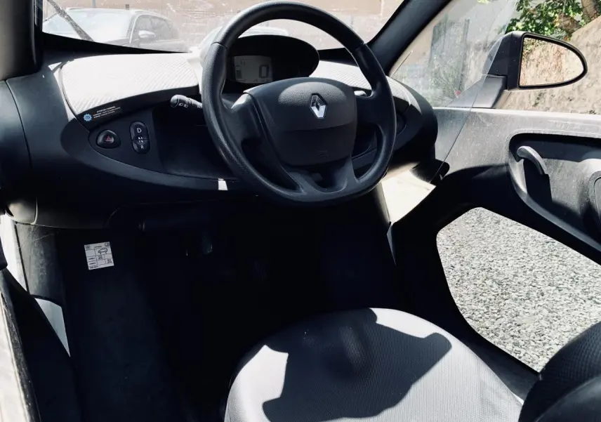 Vue intérieure côté conducteur du tableau de bord et volant noir avec logo Renault d'une Renault Twizy blanche.