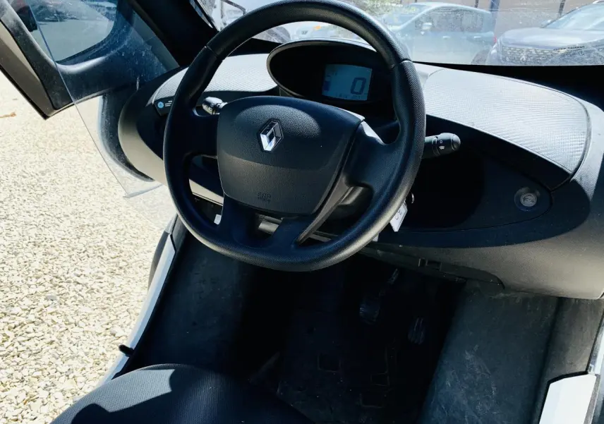 Vue intérieure centrée sur le volant noir et le tableau de bord digital d'une Renault Twizy blanche 2019.