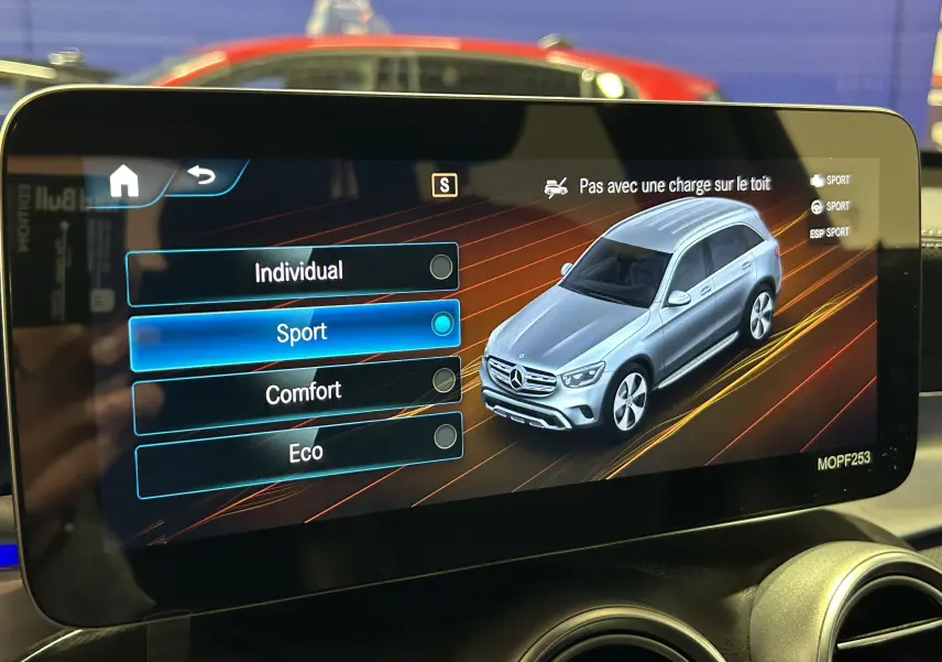 Écran intérieur montrant le menu de modes de conduite avec une Mercedes GLC vue en 3/4 avant gris argent sur l'affichage numérique.