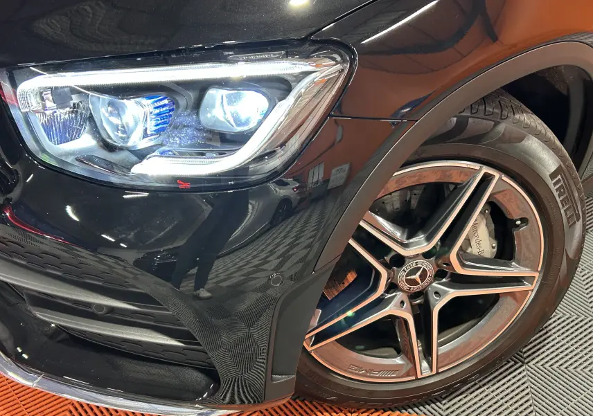 Gros plan sur l'avant droit noir métallisé du Mercedes GLC 220D AMG Line, mettant en valeur le phare LED et la jante AMG.