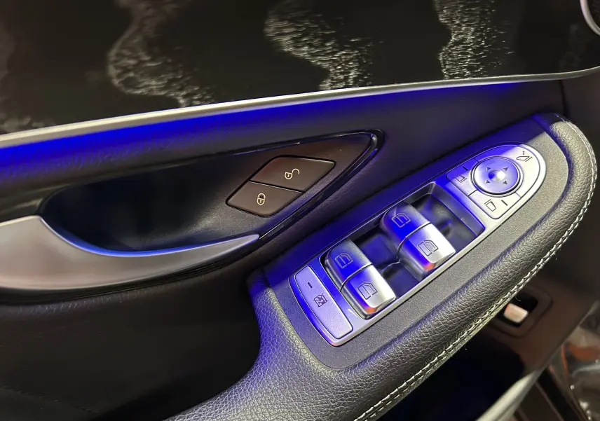 Gros plan sur la commande des vitres et la poignée de porte côté conducteur, ambiance lumineuse bleue intérieure.