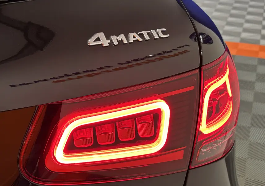 Gros plan sur le feu arrière droit allumé et l’inscription 4MATIC sur la malle arrière noire métallisée du Mercedes GLC.
