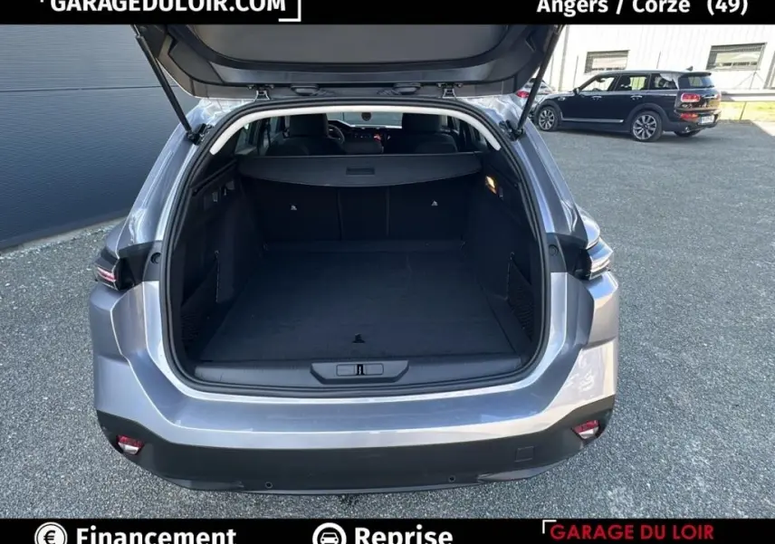 Vue arrière ouverte du coffre d'une Peugeot 308 gris clair 2023, montrant l'espace de chargement vide et le hayon levé.