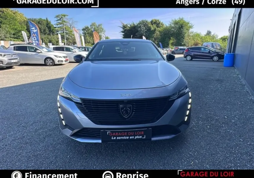 Vue avant d'une Peugeot 308 gris clair 2023 avec calandre noire et feux LED verticaux allumés.