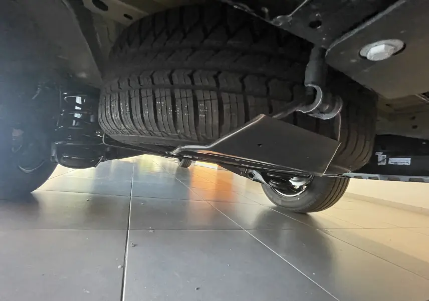 Vue en contre-plongée sous le Peugeot Traveller noir 2026, montrant la roue de secours et la suspension arrière.