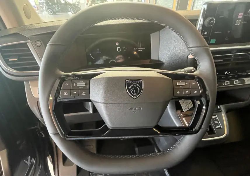 Vue rapprochée du volant cuir noir du Peugeot Traveller 2026 avec commandes intégrées et tableau de bord numérique.