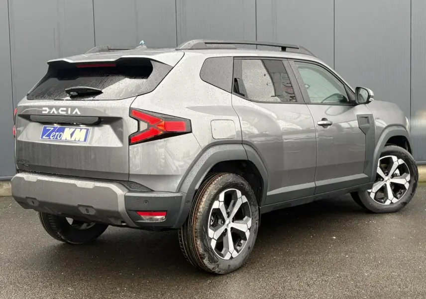 Vue 3/4 arrière droite du Dacia Duster gris schiste avec jantes alliage diamantées et barres de toit noires.