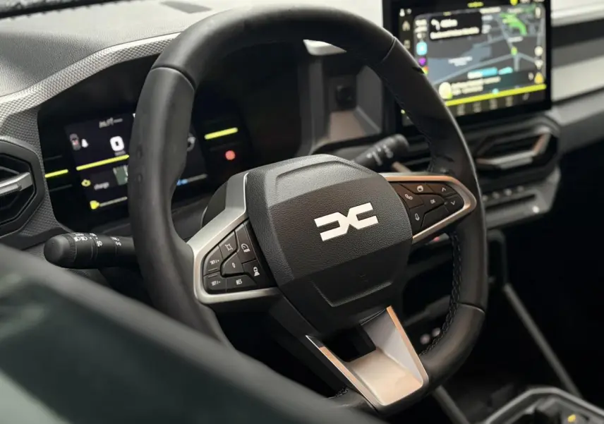 Vue rapprochée du volant noir au logo DACIA stylisé, avec tableau de bord digital et écran tactile central du Dacia Duster 2026.