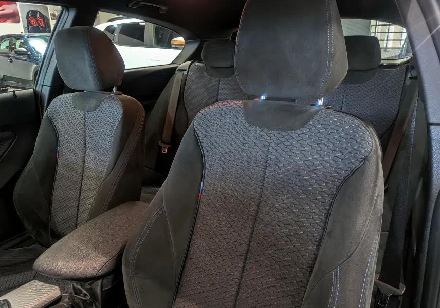 Intérieur de BMW Série 1 F21 118d M Sport 2014, vue rapprochée des sièges avant en tissu noir avec surpiqûres bleues.
