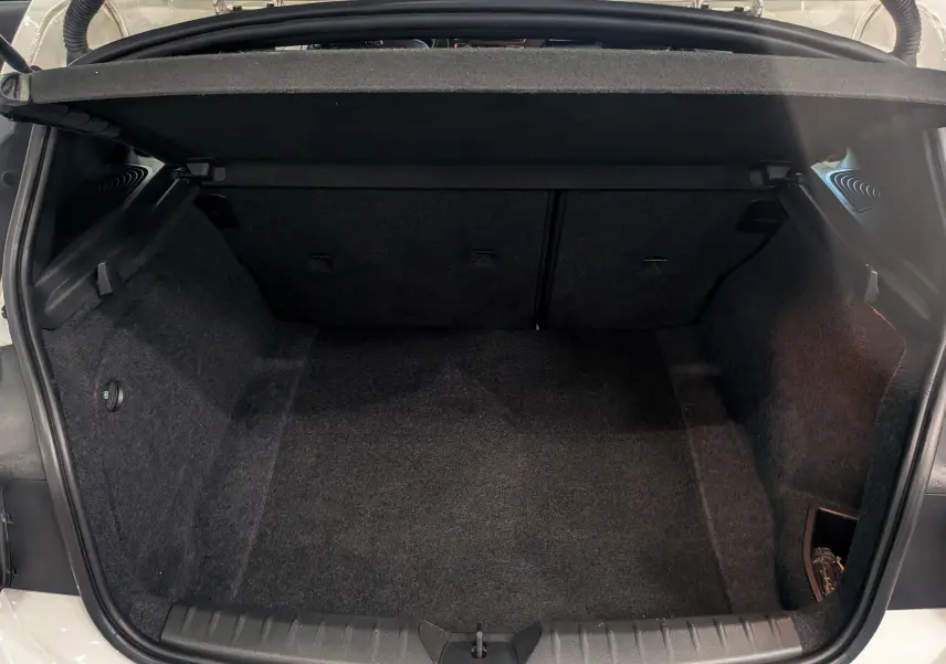 Coffre ouvert vu de l'arrière d'une BMW Série 1 F21 blanc alpin, montrant un espace de chargement propre et vide.