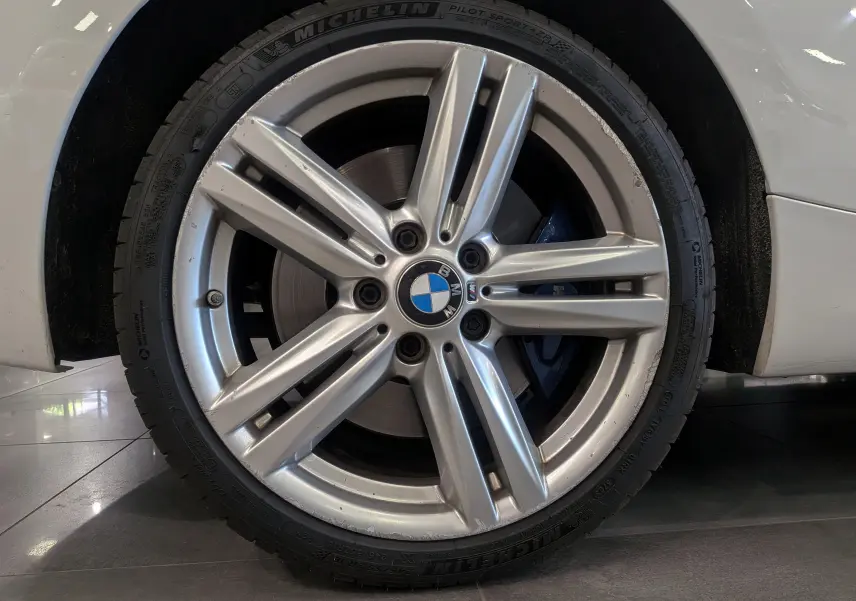 Gros plan sur la jante alliage argentée et le pneu Michelin d'une BMW Série 1 F21 blanc alpin.