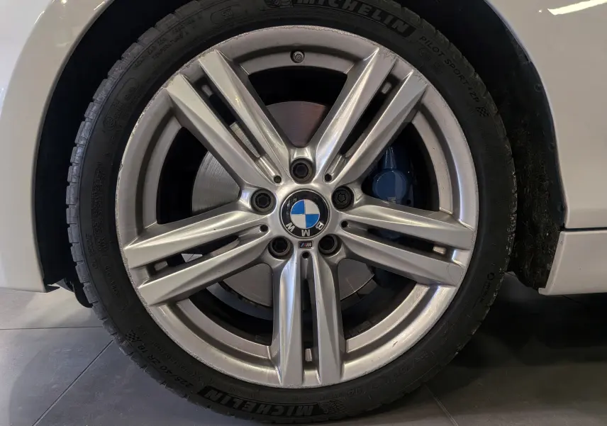 Gros plan sur la jante alliage 18 pouces et le frein bleu d'une BMW Série 1 F21 blanche Alpine côté avant droit.