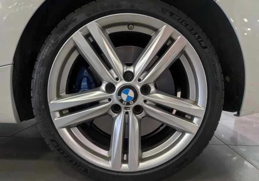Gros plan sur la jante alliage argentée avec logo BMW et étrier de frein bleu sur roue avant droite d'une BMW Série 1 blanche.